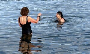 Two women in the ocean, one having just dunked